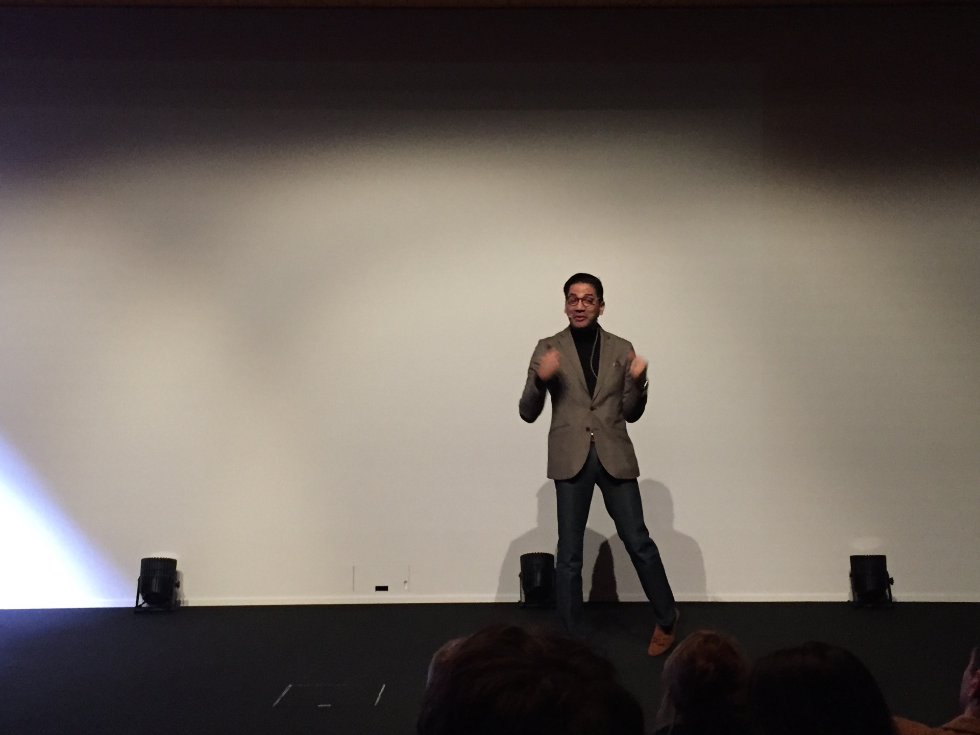 José Namén giving a keynote on a large stage in front of a white screen, seen from the audience.